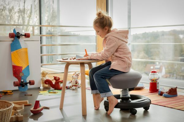 Kind sitzt auf Swoppster am Tisch und malt